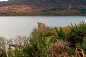 Breathtaking view of Urquhart Castle by Loch Ness surrounded by lush greenery and autumn colors.